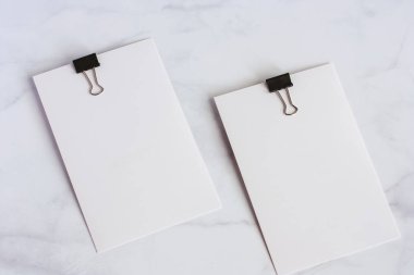 Ofis ve okul malzemeleri kavramı için beyaz kağıt kartı beyaz mermer zemin üzerinde bağlayıcı klibi