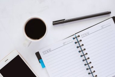 Ofis malzemeleri açılan spiral defter, kalem, bardak kahve ve beyaz mermer arka planda çalışma alanı kavramı için smartphone ile