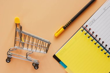 Mini alışveriş sepeti ya da bej renk arka plan planı kavramı geçirmek için üzerinde açılan spiral defter ve kalem ile arabası