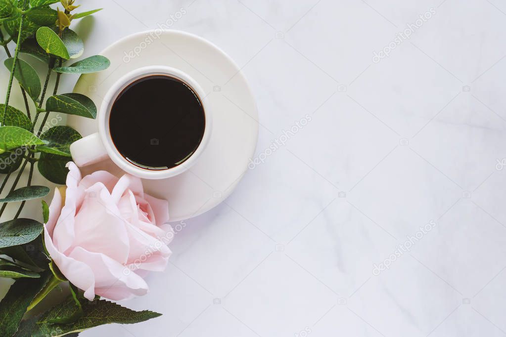 Cup of coffee with saucer and sweet pink rose on white marble background for drinks and beverage concept