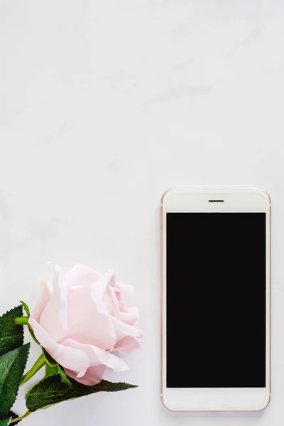 Medya teknoloji ve modern yaşam kavramı (Dikey görüntü için beyaz mermer zemin üzerine tatlı pembe gül ile Smartphone)