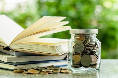 Bulanık doğal yeşil arka plan için kaydetme para ve eğitim mali kavramı karşı açılan kitap yığını ile para sikke cam kavanoz