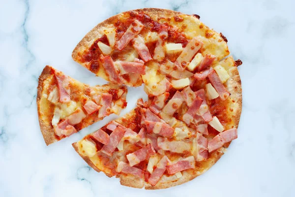 Delicious pizza with pineapple, ham slice, bacon slice, mozzarella cheese, pizza sauce on white marble background for fast food and ready to eat concept