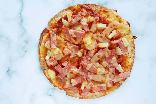 Delicious pizza with pineapple, ham slice, bacon slice, mozzarella cheese, pizza sauce on white marble background for fast food and ready to eat concept