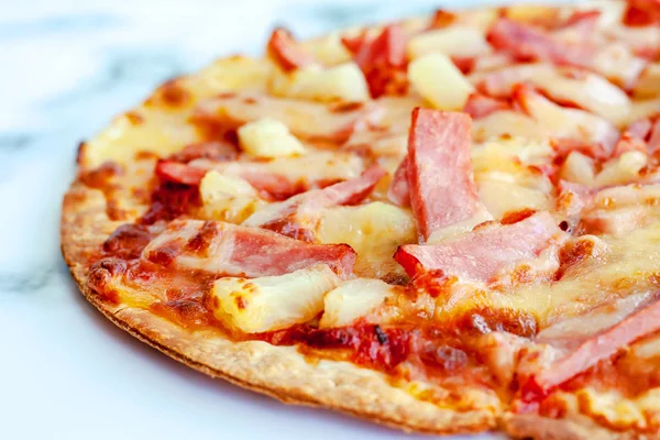 Delicious pizza with pineapple, ham slice, bacon slice, mozzarella cheese, pizza sauce on white marble background for fast food and ready to eat concept