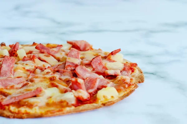 Delicious pizza with pineapple, ham slice, bacon slice, mozzarella cheese, pizza sauce on white marble background for fast food and ready to eat concept