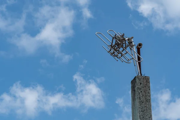 Broken aluminium TV antenna on a concrete pole with clouds and sky