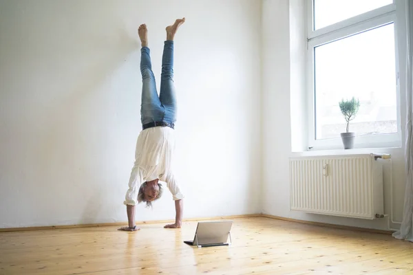 Mature Man Doing Handstand Floor Empty Room Looking Tablet — Stock Photo, Image