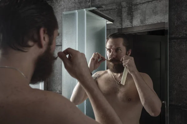 留着胡子的男人一边看着镜子 一边扭动着胡须的肖像 — 图库照片