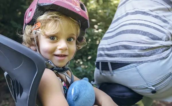 父親と一緒に自転車のチャイルドシートにヘルメットをかぶった少女の肖像画 — ストック写真