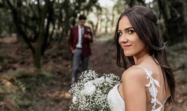 Retrato Noiva Sorridente Segurando Buquê Flores Floresta Com Noivo Fundo — Fotografia de Stock