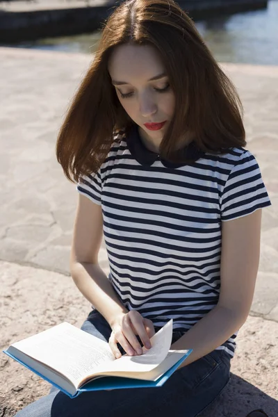 壁に座って本を読んでいる若い女性の肖像画 — ストック写真