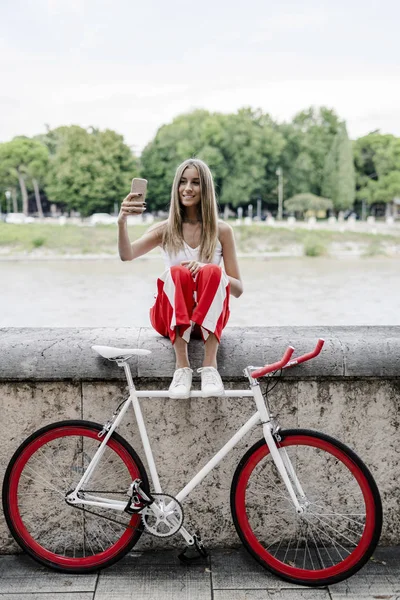 Nastoletni Dziewczyna Siedzi Riverside Obok Roweru Biorąc Selfie — Zdjęcie stockowe