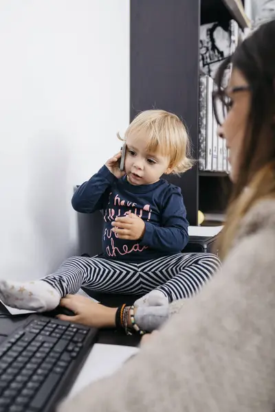 Madre Trabajando Casa Con Hija Pequeña Sentada Escritorio Sosteniendo Teléfono — Foto de Stock