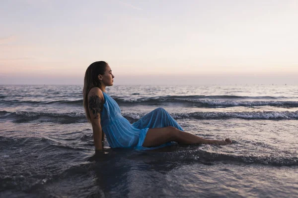 Молодая Татуированная Женщина Синем Платье Сидит Воде Берегу Моря Смотрит — стоковое фото