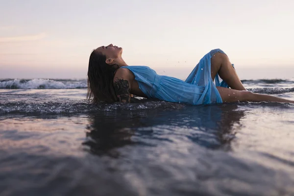 Młoda Wytatuowana Kobieta Niebieskiej Sukience Leżąca Wodzie Nad Brzegiem Morza — Zdjęcie stockowe