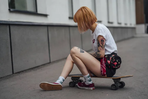 年轻女子坐在人行道上的雕刻滑板上 — 图库照片