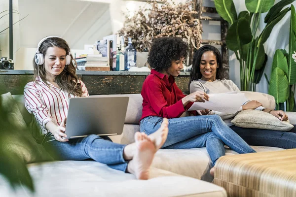 Tre donne con computer portatile e documenti seduti sul divano — Foto stock