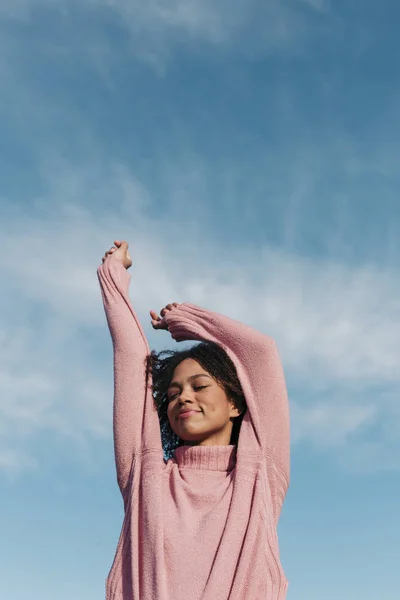 Porträt einer lächelnden jungen Frau mit rosa Pullover gegen den Himmel — Stockfoto
