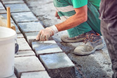 Bir işçi 's eldivenli elleri çekiç taş döşeme eklemenizi sağlar. İşçi kaldırım Arnavut kaldırımı taşları ve granit taşlar kullanarak oluşturma.