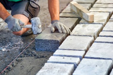 Bir işçi 's eldivenli elleri çekiç taş döşeme eklemenizi sağlar. İşçi kaldırım Arnavut kaldırımı taşları ve granit taşlar kullanarak oluşturma.