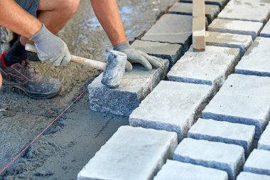 Bir işçi 's eldivenli elleri çekiç taş döşeme eklemenizi sağlar. İşçi kaldırım Arnavut kaldırımı taşları ve granit taşlar kullanarak oluşturma.