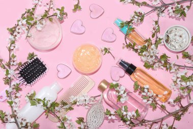 Spa malzemeleri, pembe arka planda çiçek açan kiraz dallarıyla cilt ve vücut bakımı için kremler. Alışveriş konsepti ve modern kadın, satış, üst görünüm, seçici odaklanma