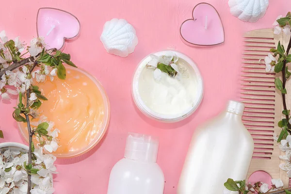 Spa ingredients, a set of creams for skin and body care on a pink background with branches of blooming cherry. Shopping concept and modern woman, sale, top view, selective focus