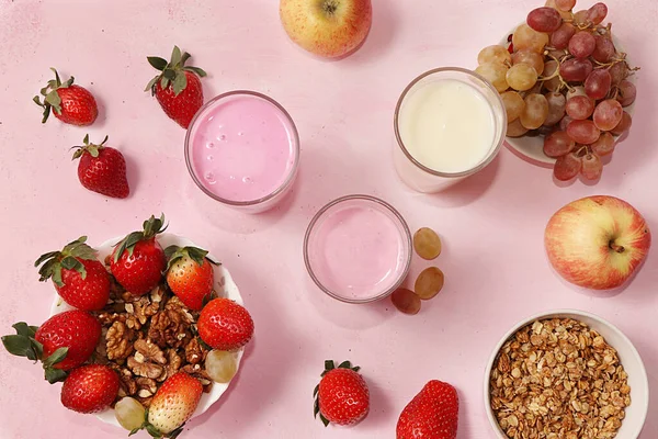 Strawberry and apple smoothies and granola, granola, fresh berries, apples, strawberries and grapes on a pink sunny background. The concept of healthy and natural food. Healthy breakfast, food for children, selective focus, top view