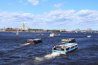 Rusya, Petersburg, 29 Haziran 2019. Vasilyevsky Adası 'nın tükürüğü. Fotoğraf, Neva kıyısında gökyüzüne karşı Peter ve Paul Kalesi 'ni ve şehir manzarasına hayran turistlerle dolu bir eğlence teknesini gösteriyor..