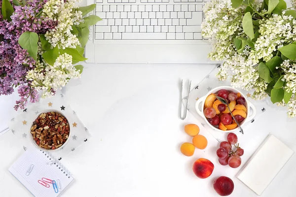 Desktop of a modern woman, home office, fruit salad with granola, grapes and peaches on a light table. Healthy breakfast with ingredients, healthy lifestyle concept,