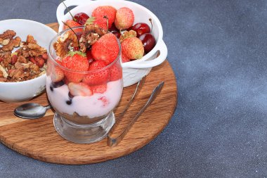İçinde malzemeler olan sağlıklı bir kahvaltı, çocuklar için yiyecek, çilekli yoğurt, meyve püresi ve granola, beton bir masada çilek. Sağlıklı ve doğal gıda kavramı