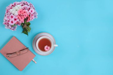 Modern kadın masaüstü, merkez ofis. Mavi bir masada bir fincan çay, bir defter ve çiçekler. Yaşam tarzı konsepti, düz konum, metin konumu, sonbahar minimal bileşimi