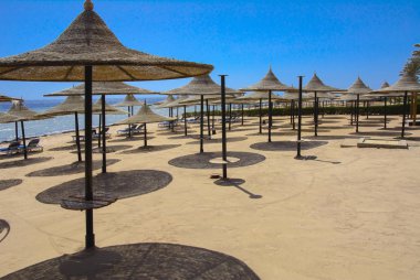 Hasır şemsiyeler aşırı ısınma ve mavi gökyüzü ve mavi denizin karşı bir kumlu plajda şezlong karşı korumak için bir satır. Yaz tatil, turizm, seyahat kavramı.