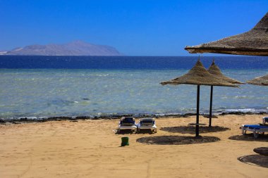 Hasır şemsiyeler aşırı ısınma ve mavi gökyüzü ve mavi denizin karşı bir kumlu plajda şezlong karşı korumak için bir satır. Yaz tatil, turizm, seyahat kavramı.