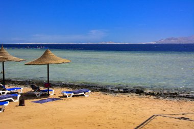 Sharm el-Sheikh, Mısır - 14 Mart 2018. Bir dizi karşı bir mavi gökyüzü ve mavi deniz kumlu bir plaj üzerinde aşırı ısınma karşı korumak için hasır şemsiyeler. Yaz tatil, turizm, seyahat kavramı.
