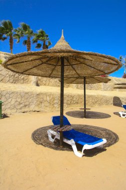 Hasır şemsiyeler aşırı ısınma ve mavi gökyüzü ve mavi denizin karşı bir kumlu plajda şezlong karşı korumak için bir satır. Yaz tatil, turizm, seyahat kavramı.