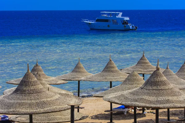 Sharm el-Sheikh, Mısır - 14 Mart 2018. Bir dizi karşı bir mavi gökyüzü ve mavi deniz kumlu bir plaj üzerinde aşırı ısınma karşı korumak için hasır şemsiyeler. Yaz tatil, turizm, seyahat kavramı.