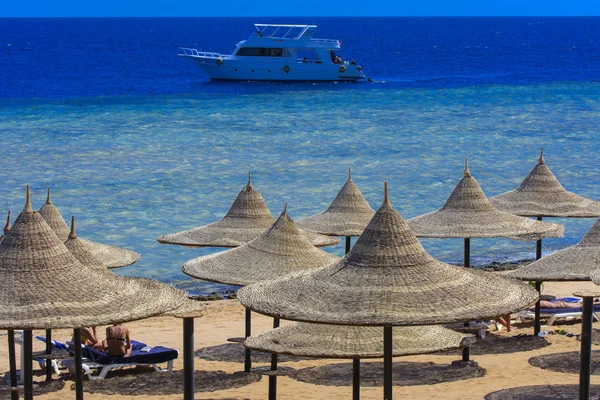 Sharm el-Sheikh, Mısır - 14 Mart 2018. Bir dizi karşı bir mavi gökyüzü ve mavi deniz kumlu bir plaj üzerinde aşırı ısınma karşı korumak için hasır şemsiyeler. Yaz tatil, turizm, seyahat kavramı.