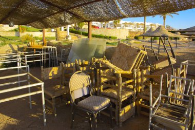 Plaj mobilya boş bir sahil sarı kum ve mavi gökyüzünün bir arka plan üzerinde terk edilmiş. Atılmış, gereksiz şeyler. Tatil, turizm.