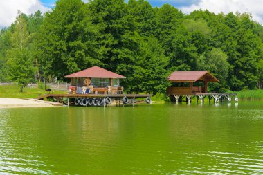 Ağaçlar ve sazlık bulutlar mavi gökyüzü karşı kıyısında çevrili bir nehir ortasından bir manzara güzel bir görüntüsü. Ahşap çardak sahilde. Yansıma, su, Turizm hedef