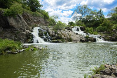 Yoluyla ve liken ve moss bir arka plan mavi bir gökyüzü ve yeşil bitki örtüsü ile kaplı kaya şelale Nehri akar.