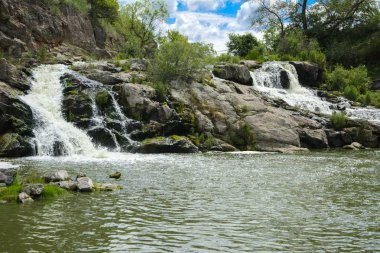 Yoluyla ve liken ve moss bir arka plan mavi bir gökyüzü ve yeşil bitki örtüsü ile kaplı kaya şelale Nehri akar.