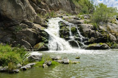 Yoluyla ve liken ve moss bir arka plan mavi bir gökyüzü ve yeşil bitki örtüsü ile kaplı kaya şelale Nehri akar.