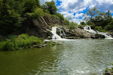 Yoluyla ve liken ve moss bir arka plan mavi bir gökyüzü ve yeşil bitki örtüsü ile kaplı kaya şelale Nehri akar.