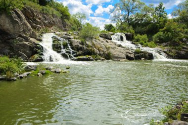 Yoluyla ve liken ve moss bir arka plan mavi bir gökyüzü ve yeşil bitki örtüsü ile kaplı kaya şelale Nehri akar.