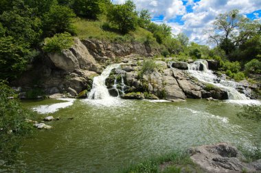 Yoluyla ve liken ve moss bir arka plan mavi bir gökyüzü ve yeşil bitki örtüsü ile kaplı kaya şelale Nehri akar.
