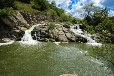 Yoluyla ve liken ve moss bir arka plan mavi bir gökyüzü ve yeşil bitki örtüsü ile kaplı kaya şelale Nehri akar.