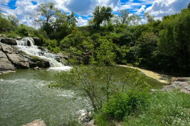 Yoluyla ve liken ve moss bir arka plan mavi bir gökyüzü ve yeşil bitki örtüsü ile kaplı kaya şelale Nehri akar.