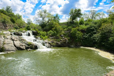 Yoluyla ve liken ve moss bir arka plan mavi bir gökyüzü ve yeşil bitki örtüsü ile kaplı kaya şelale Nehri akar.